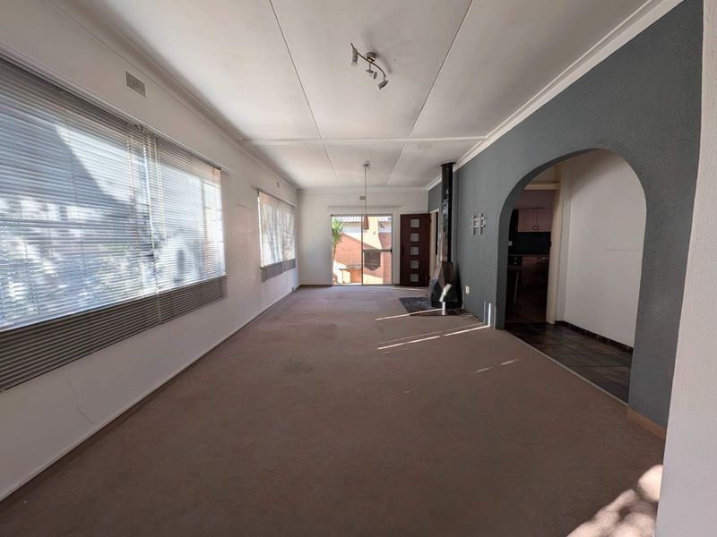 Spacious, empty living room featuring a freestanding fireplace, arched entryway, and large windows with venetian blinds, offering a blank canvas for renovation.