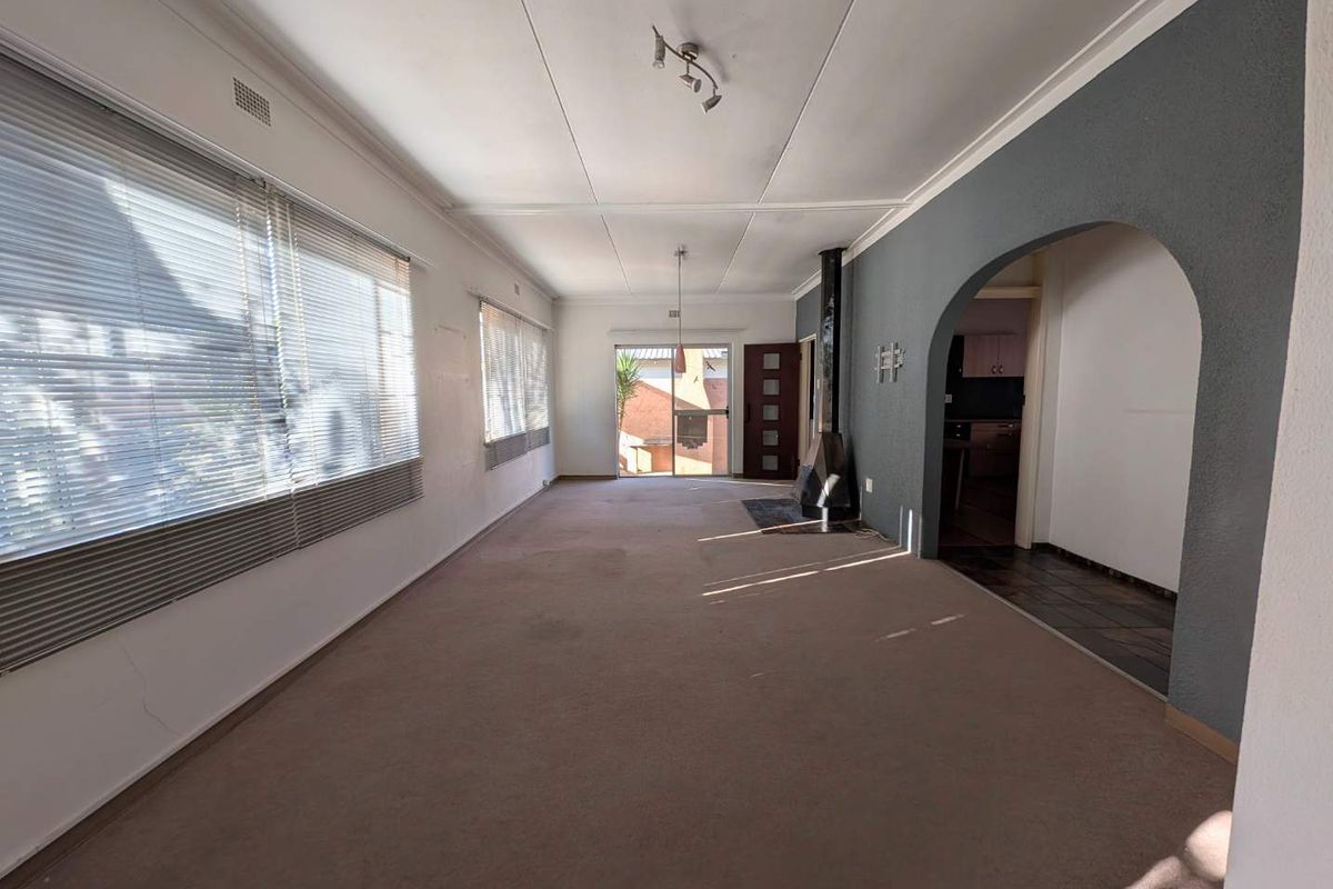 Spacious, empty living room featuring a freestanding fireplace, arched entryway, and large windows with venetian blinds, offering a blank canvas for renovation.