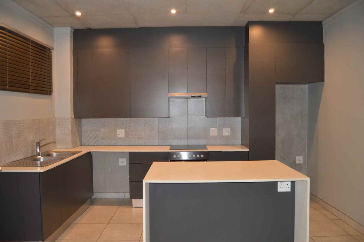 Modern kitchen featuring dark grey cabinetry, a central island, integrated oven and hob, and a tiled backsplash in an open-plan layout.