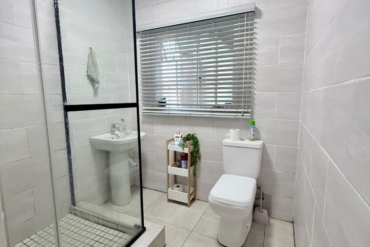 A functional bathroom featuring a glass-enclosed shower, pedestal basin, and toilet with tiled walls and flooring.