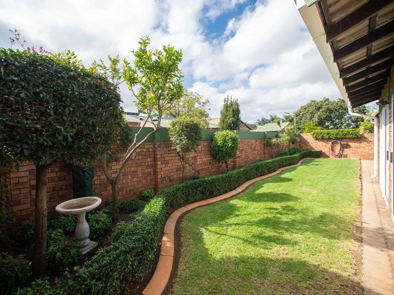 A well-maintained rear garden featuring a manicured lawn, established hedging, and a brick boundary wall, adjacent to a covered patio area.