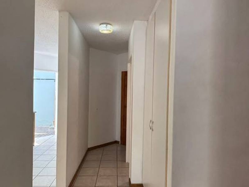 A clean, tiled hallway featuring built-in storage cupboards and access to a wooden staircase, leading towards an outdoor area.