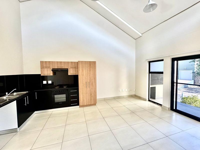 Modern open-plan kitchen and living area featuring high vaulted ceilings, sleek two-tone cabinetry, tiled floors, and direct access to an outdoor patio.