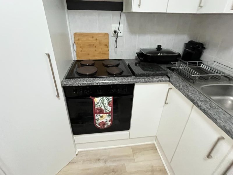 Compact kitchen featuring a built-in oven, electric hob, extractor fan, laminate countertops, and a stainless steel sink with tiled backsplash.