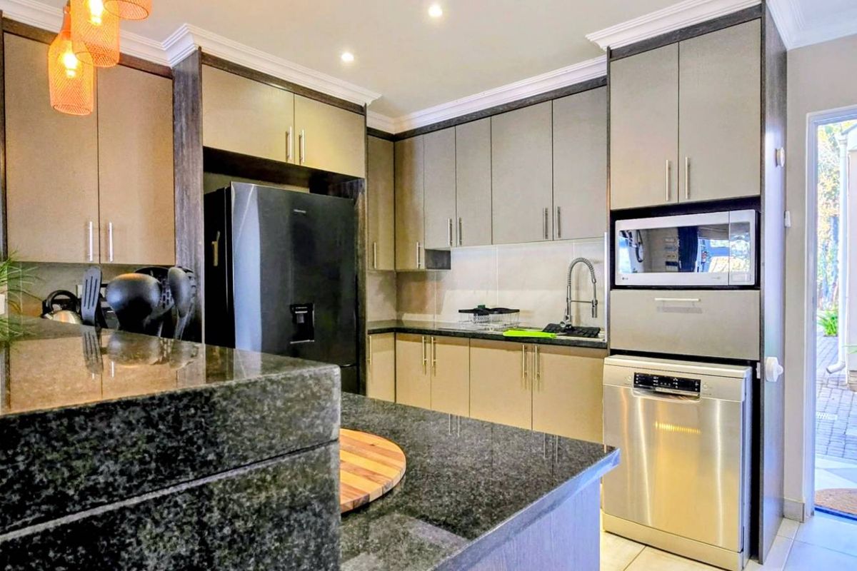 Modern kitchen featuring granite countertops, sleek cabinetry, integrated microwave, and stainless steel dishwasher, with direct access to an outdoor area.