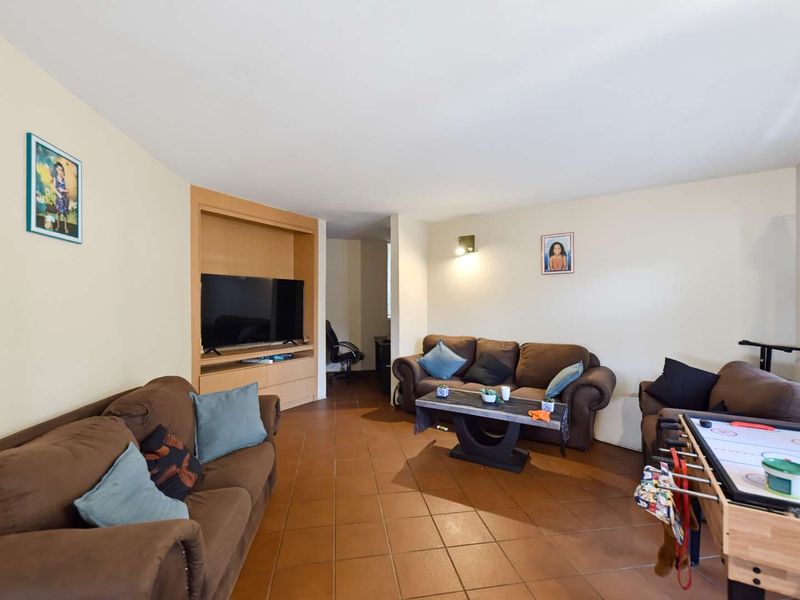 A spacious living room featuring terracotta floor tiles and a built-in media cabinet, offering a functional layout for relaxation and entertainment.