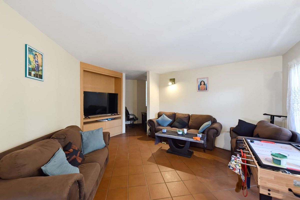 A spacious living room featuring terracotta floor tiles and a built-in media cabinet, offering a functional layout for relaxation and entertainment.