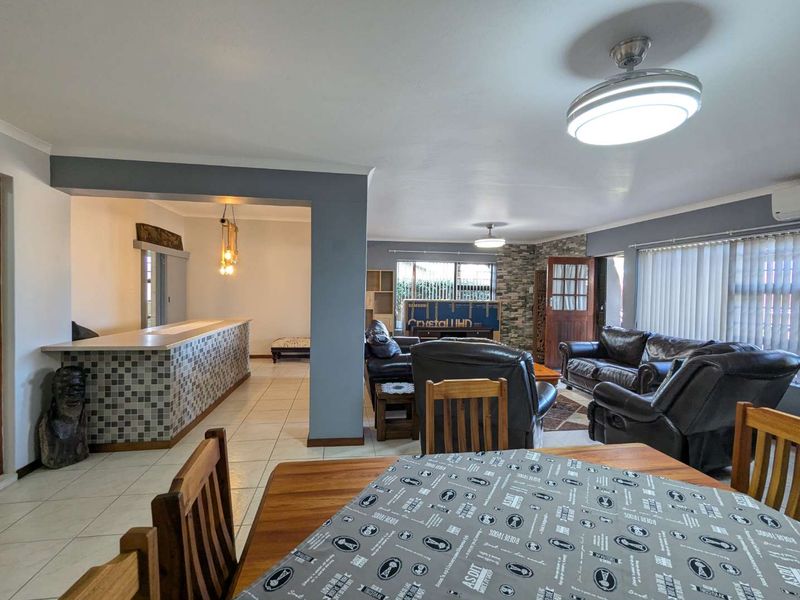 Spacious open-plan living and dining area featuring tiled flooring, a breakfast bar, and a stone feature wall, offering a versatile layout for family living.