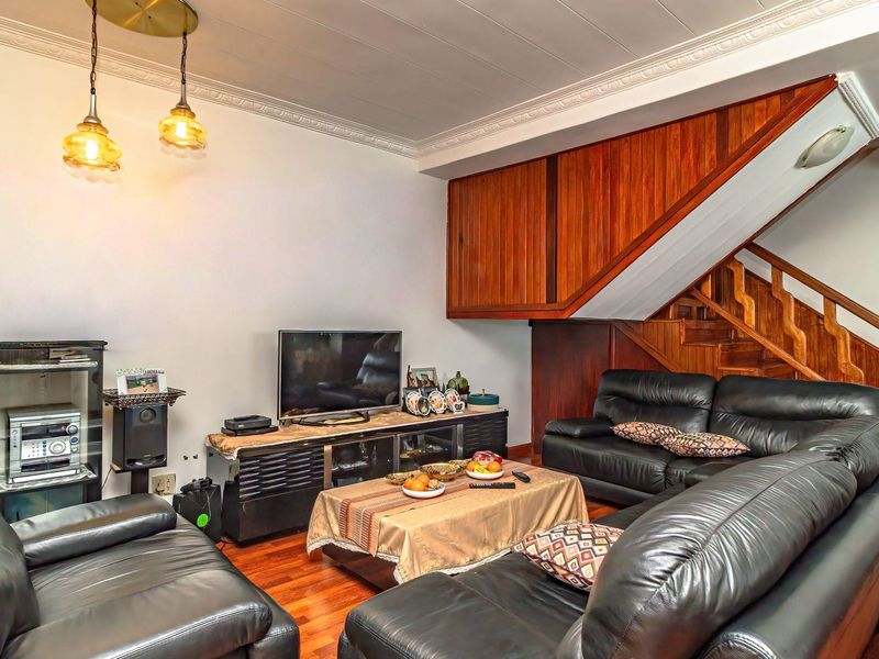 A cozy living room featuring warm hardwood flooring, a prominent wooden staircase, and decorative ceiling cornicing, creating a traditional and inviting atmosphere.