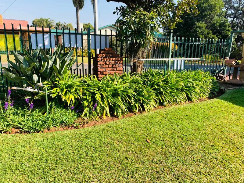 A well-maintained garden area featuring a manicured lawn, established garden beds, and secure metal perimeter fencing.