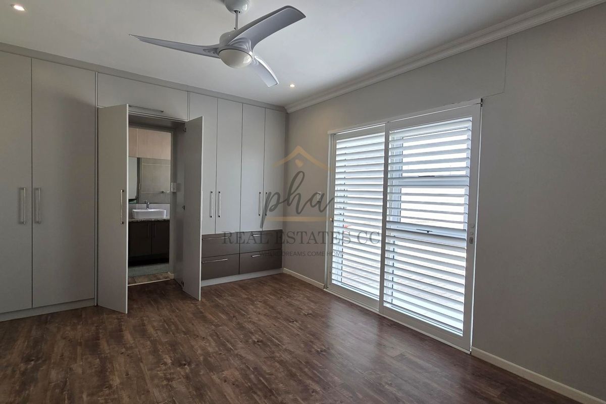 Spacious bedroom featuring modern built-in cupboards, laminate flooring, a ceiling fan, and sliding doors with fitted blinds leading to the exterior.