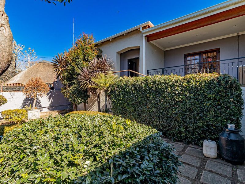 Rear exterior view featuring a covered patio with wrought iron railings, paved walkway, and established garden landscaping.