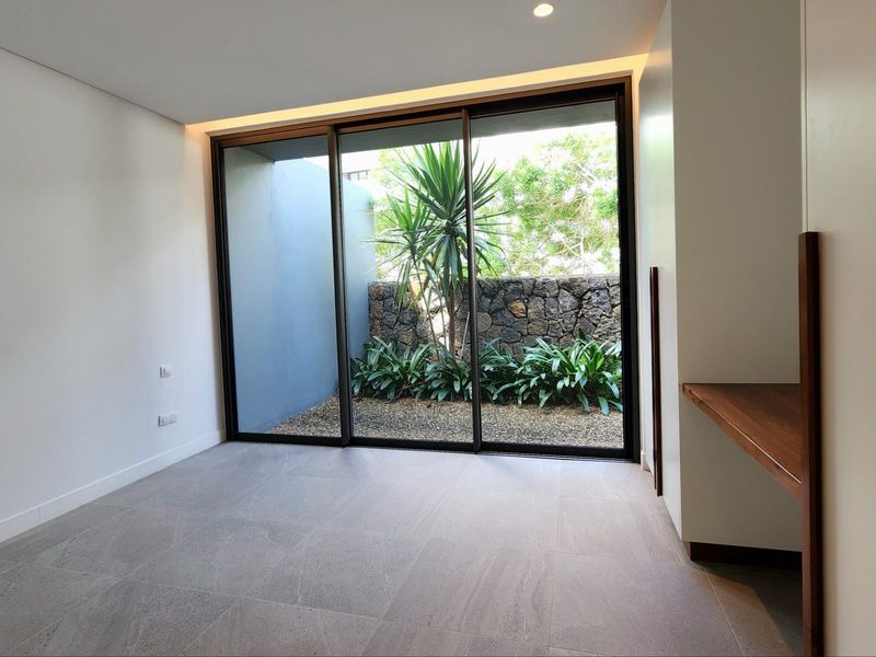 A bright, modern bedroom featuring large sliding glass doors that open onto a private, landscaped courtyard with stone wall detailing.