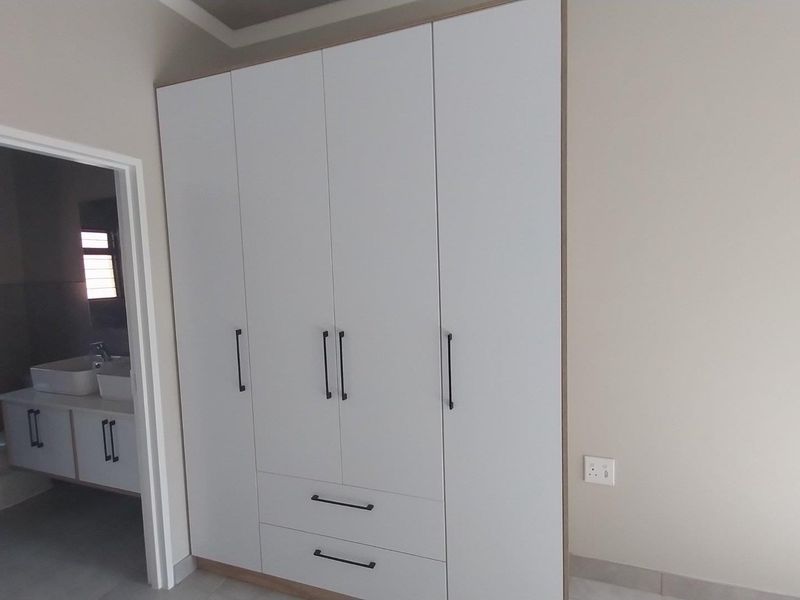 A clean bedroom featuring a modern built-in wardrobe with white cabinetry and black hardware, with an adjacent view into an en-suite bathroom.