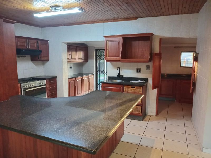 Spacious kitchen featuring granite countertops, extensive wooden cabinetry, a freestanding oven, and a separate scullery area with tiled flooring throughout.