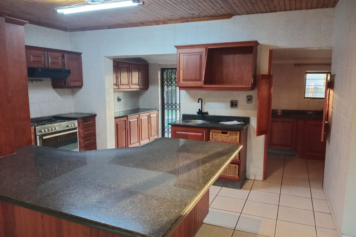 Spacious kitchen featuring granite countertops, extensive wooden cabinetry, a freestanding oven, and a separate scullery area with tiled flooring throughout.