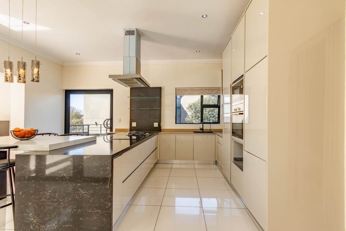 Modern kitchen featuring high-gloss cabinetry, stone countertops, a central island, built-in oven, and stainless steel extractor fan with tiled flooring.
