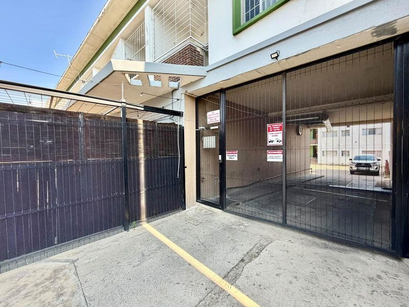 Front entrance area featuring a secure gated access point, concrete driveway, and building facade with an overhead awning.
