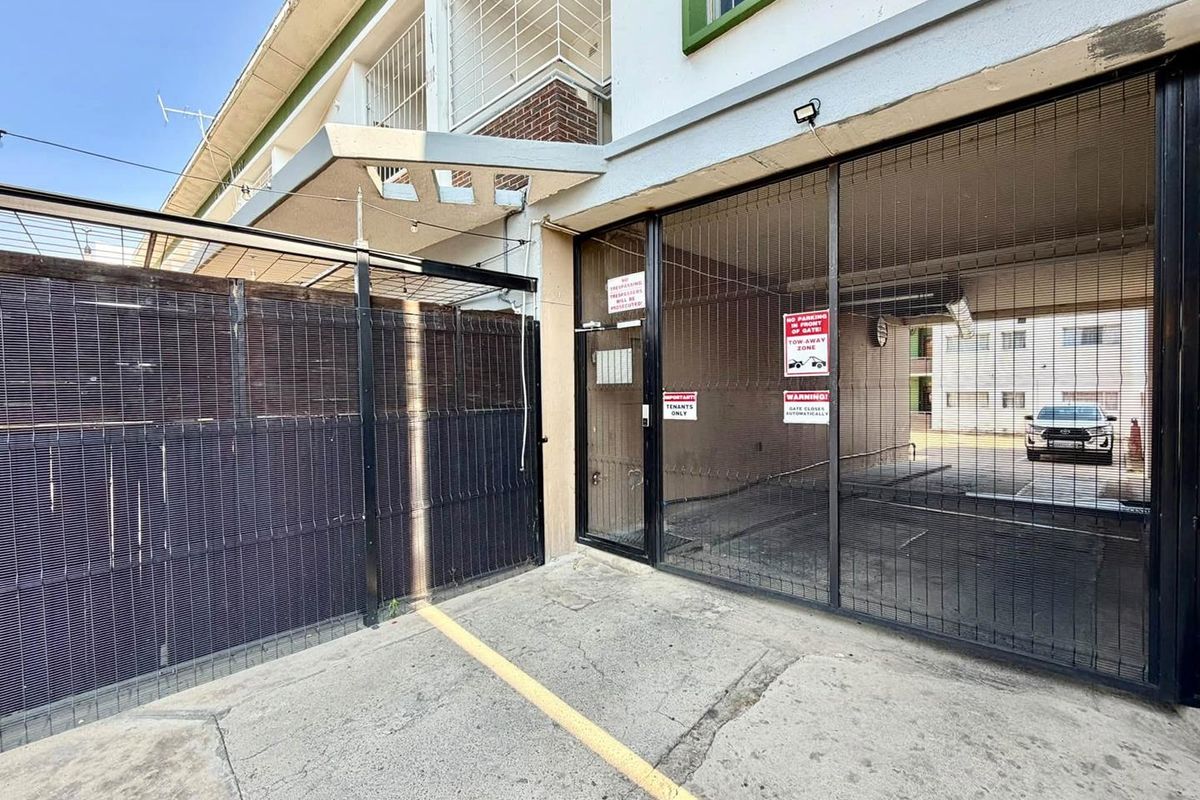 Front entrance area featuring a secure gated access point, concrete driveway, and building facade with an overhead awning.
