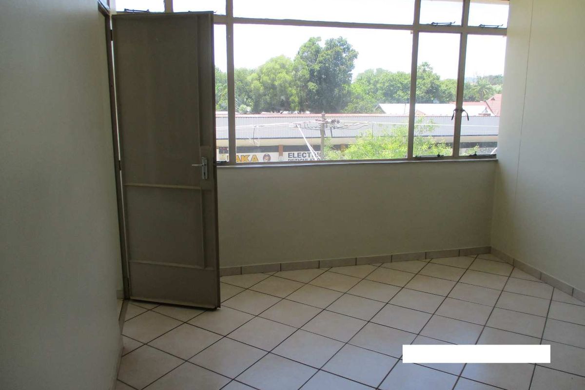 An empty bedroom featuring tiled flooring, large windows providing natural light, and a single door leading to the exterior.