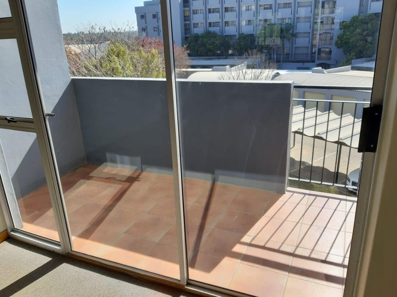 A private balcony featuring terracotta floor tiles, a solid masonry parapet wall, and a metal balustrade, accessible via large sliding glass doors.