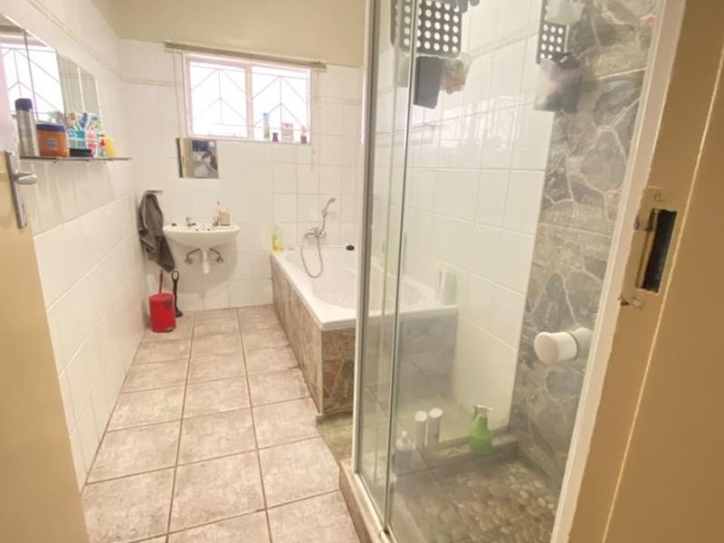 A functional bathroom featuring a separate shower enclosure, bathtub, and pedestal basin with tiled finishes, requiring some cosmetic maintenance and updates.