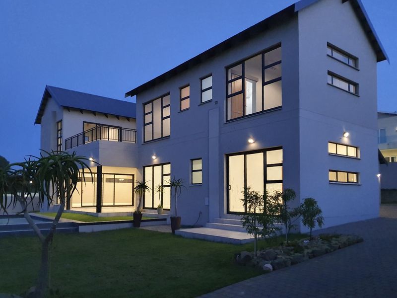 A modern double-storey residential property at dusk, featuring large glass sliding doors, a balcony, and well-maintained exterior lighting and landscaping.
