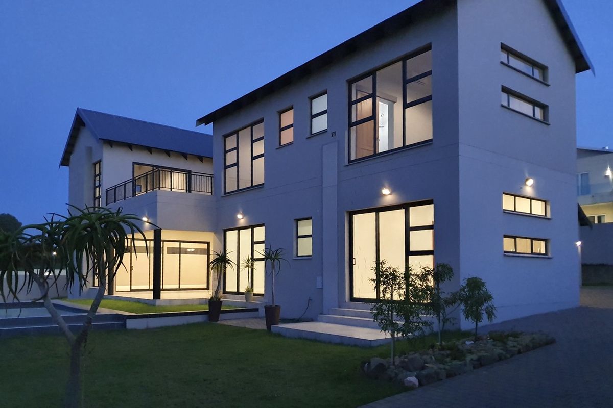 A modern double-storey residential property at dusk, featuring large glass sliding doors, a balcony, and well-maintained exterior lighting and landscaping.