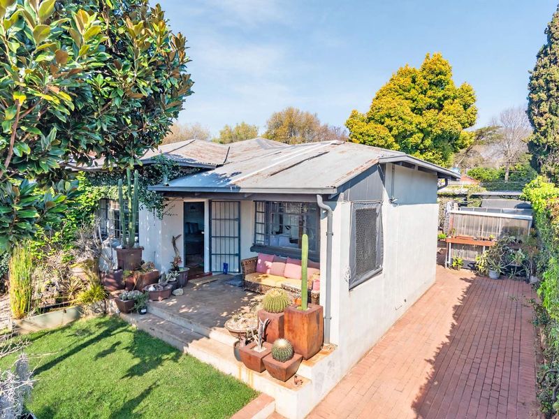 Rear view of a detached house featuring a corrugated metal roof, a paved pathway, and a small concrete patio area.