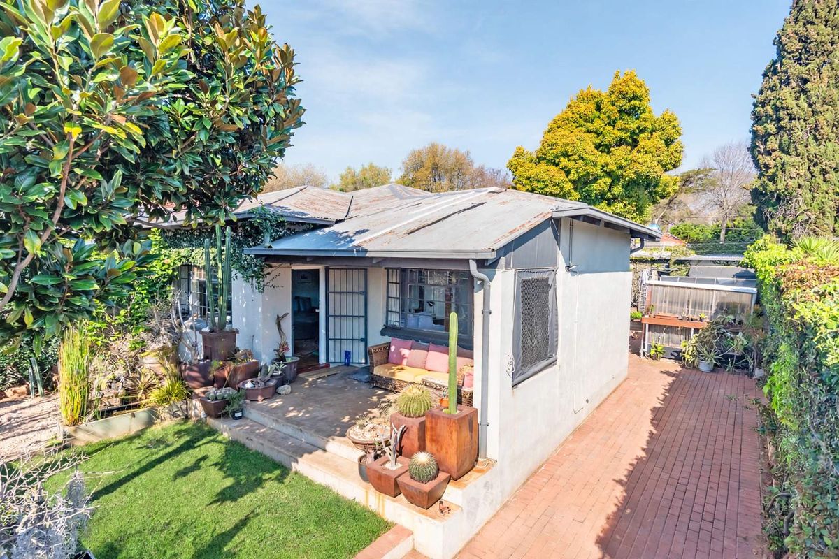 Rear view of a detached house featuring a corrugated metal roof, a paved pathway, and a small concrete patio area.