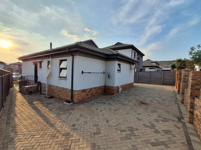 Rear view of the property featuring paved driveway, brick boundary walls, and well-maintained exterior finishes with tiled roofing.