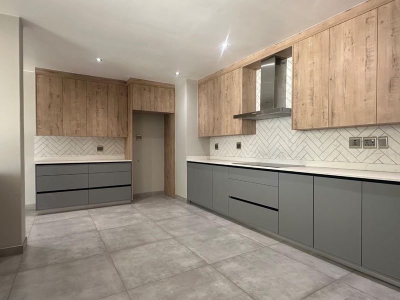Modern kitchen featuring two-tone cabinetry, stone countertops, herringbone tile backsplash, and integrated hob with stainless steel extractor fan.