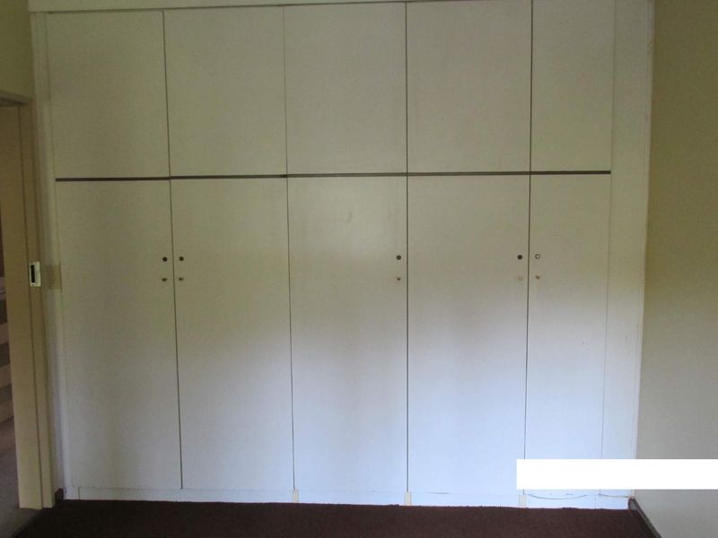 A bedroom featuring a wall of built-in cupboards with a dated finish and missing hardware, offering potential for modernization.