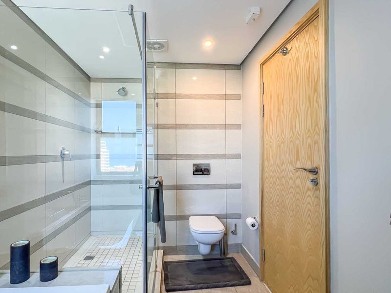 Modern bathroom featuring a glass-enclosed walk-in shower, wall-mounted toilet, and neutral tiled finishes.