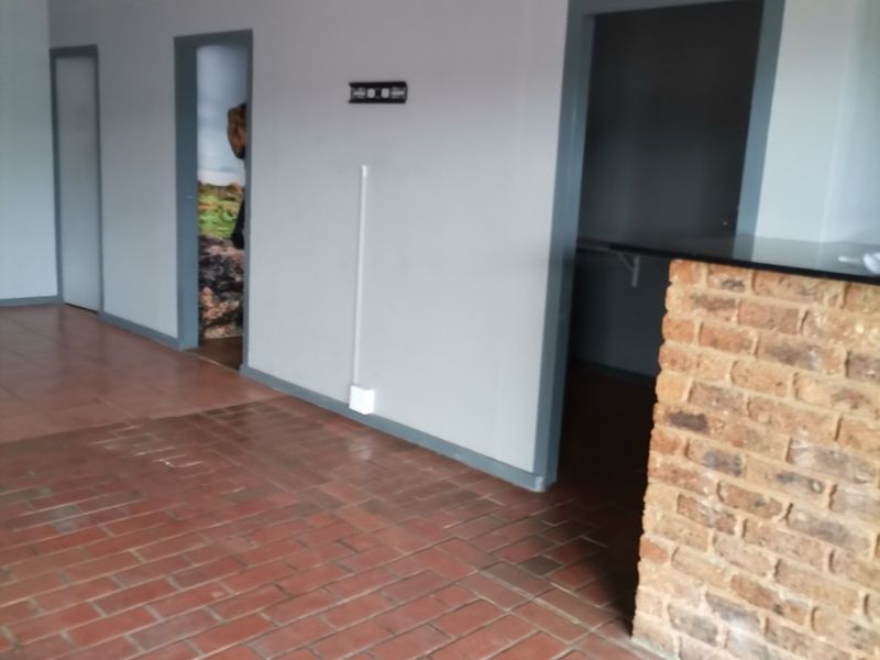 An empty living area featuring terracotta tile flooring, a brick feature wall, and multiple internal doorways, currently requiring ceiling and electrical finishing.