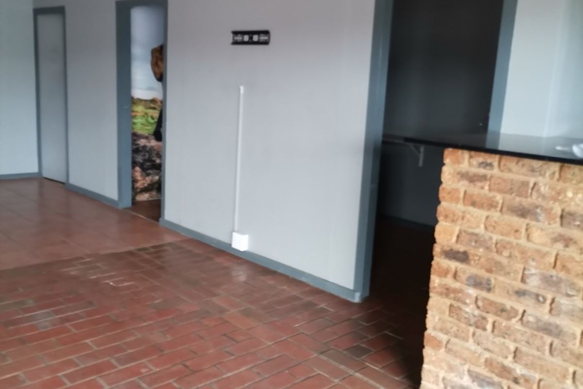 An empty living area featuring terracotta tile flooring, a brick feature wall, and multiple internal doorways, currently requiring ceiling and electrical finishing.