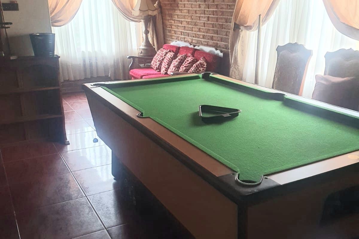 Spacious living area featuring exposed brick walls, timber ceiling, and tiled flooring, currently utilized as a games room with a pool table.