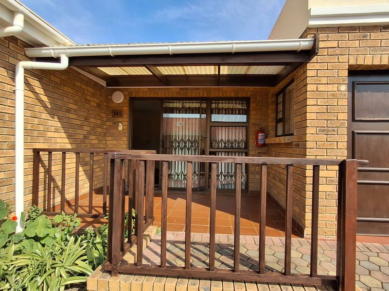 Front entrance of the townhouse featuring a covered patio area with brick facade, timber railing, and secure access gate.