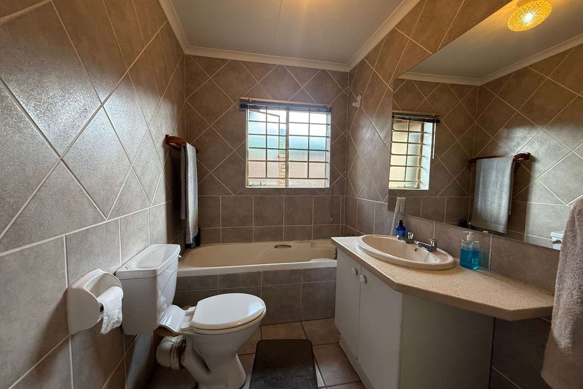 A functional bathroom featuring full-height wall tiling, a built-in vanity with a basin, a standard toilet, and a bathtub with a window.