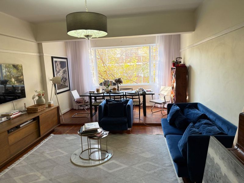 Spacious open-plan living and dining area featuring polished hardwood floors, a raised dining platform, and a large window providing natural light and garden views.