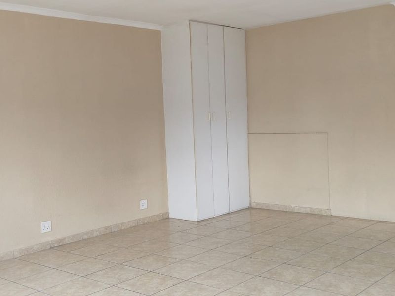 An empty open-plan living area featuring neutral wall tones, tiled flooring, and a built-in storage cupboard.