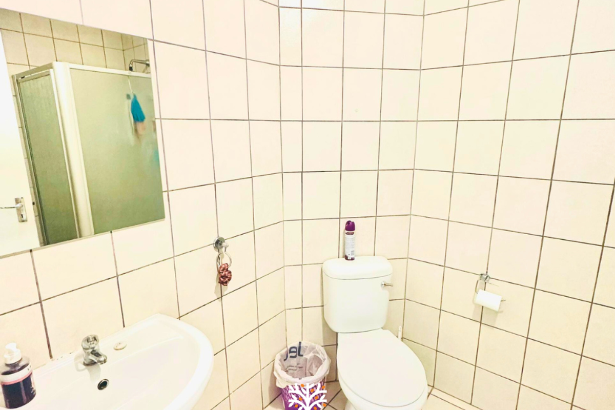 A functional bathroom featuring a pedestal basin, a standard toilet, and a shower enclosure with full-height wall tiling.