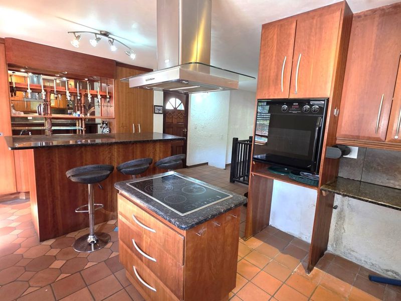 Spacious kitchen featuring wooden cabinetry, granite countertops, a central island with an electric hob, and a built-in oven with a stainless steel extractor fan.