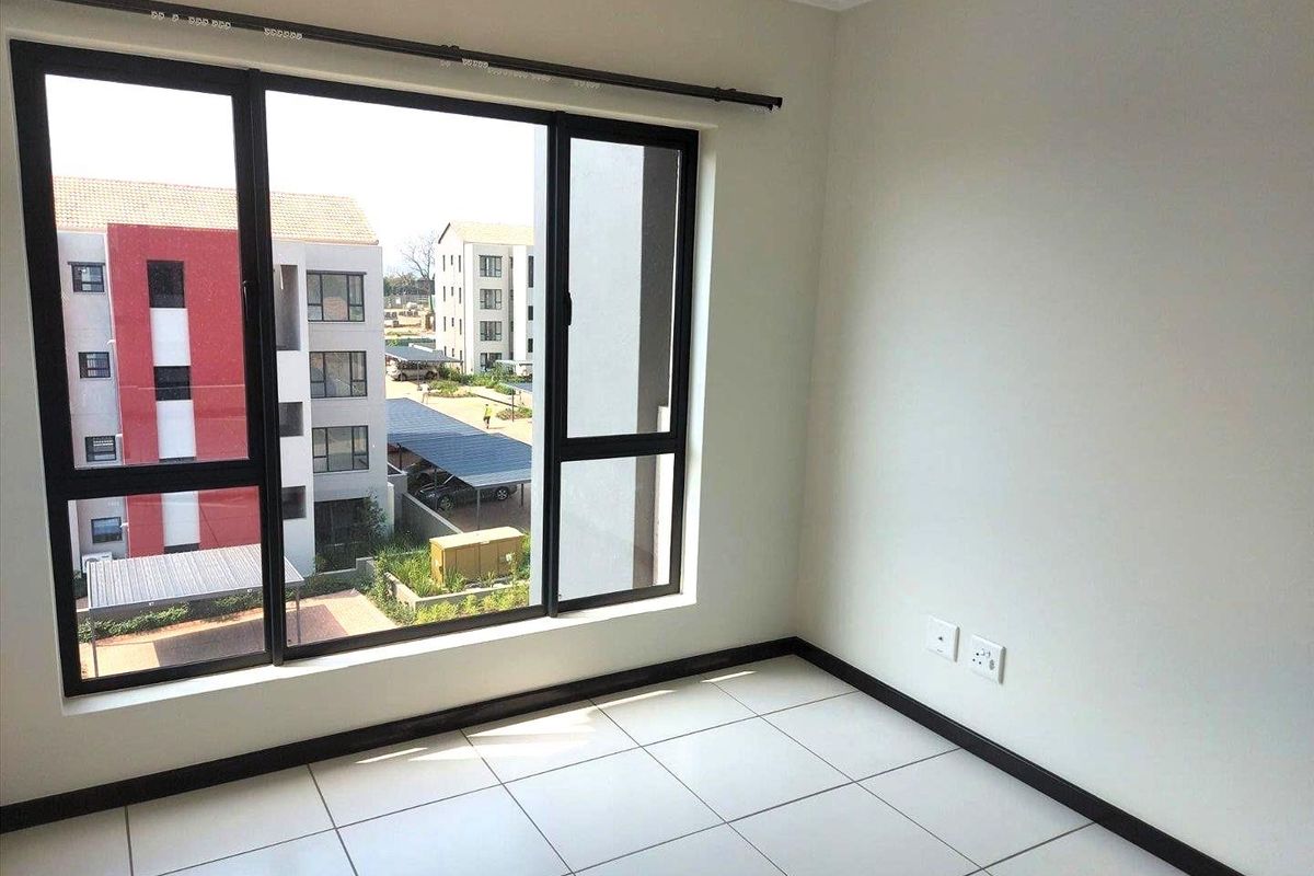 A bright, empty bedroom featuring neutral tiled flooring, modern black aluminium window frames, and clean white walls, offering a blank canvas for personalization.