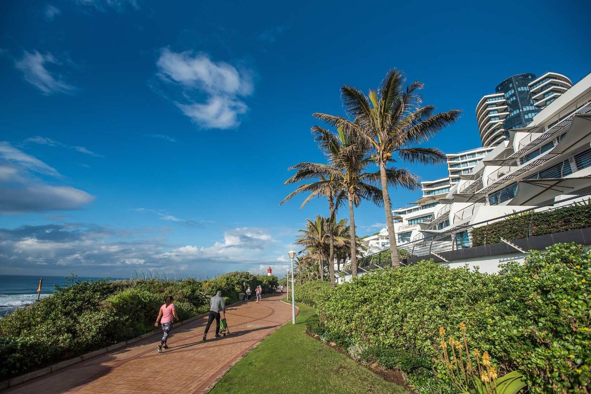 A scenic view of the apartment complex exterior, featuring landscaped gardens, paved walkways, and private balconies overlooking the coastal area.