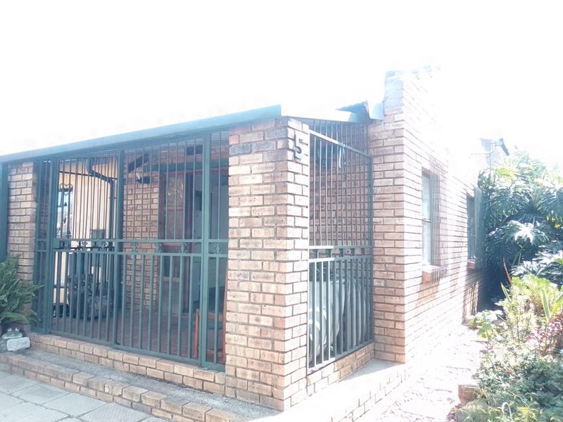 A covered patio area featuring face brick construction and security bars, showing signs of wear and structural damage at the roofline.