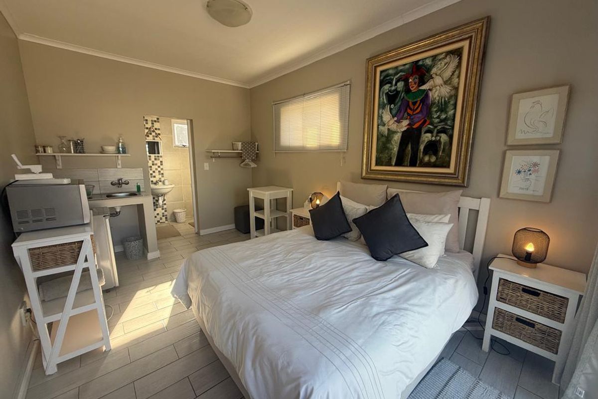 A bedroom featuring tiled flooring, a small kitchenette area with a sink, and an en-suite bathroom with mosaic tile accents.