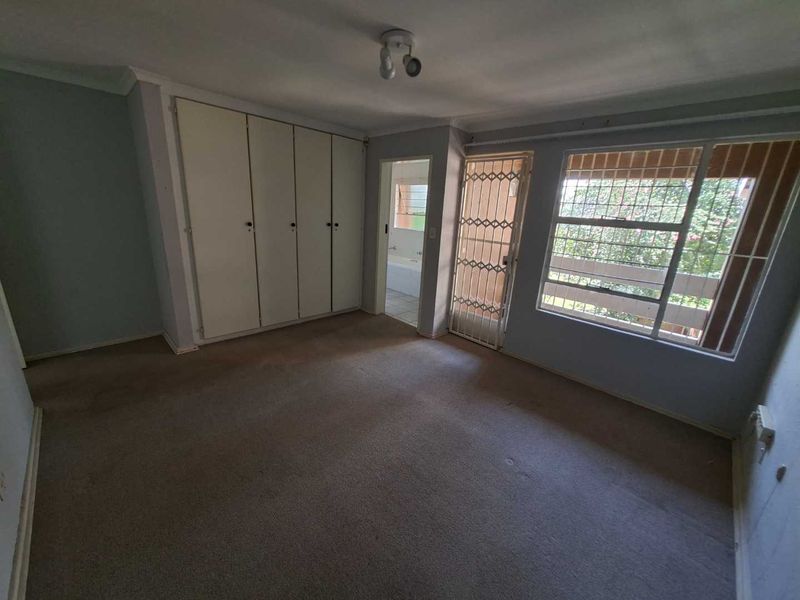 Spacious bedroom featuring built-in cupboards, carpeted flooring, and direct access to an en-suite bathroom, secured with a metal security gate and burglar bars.