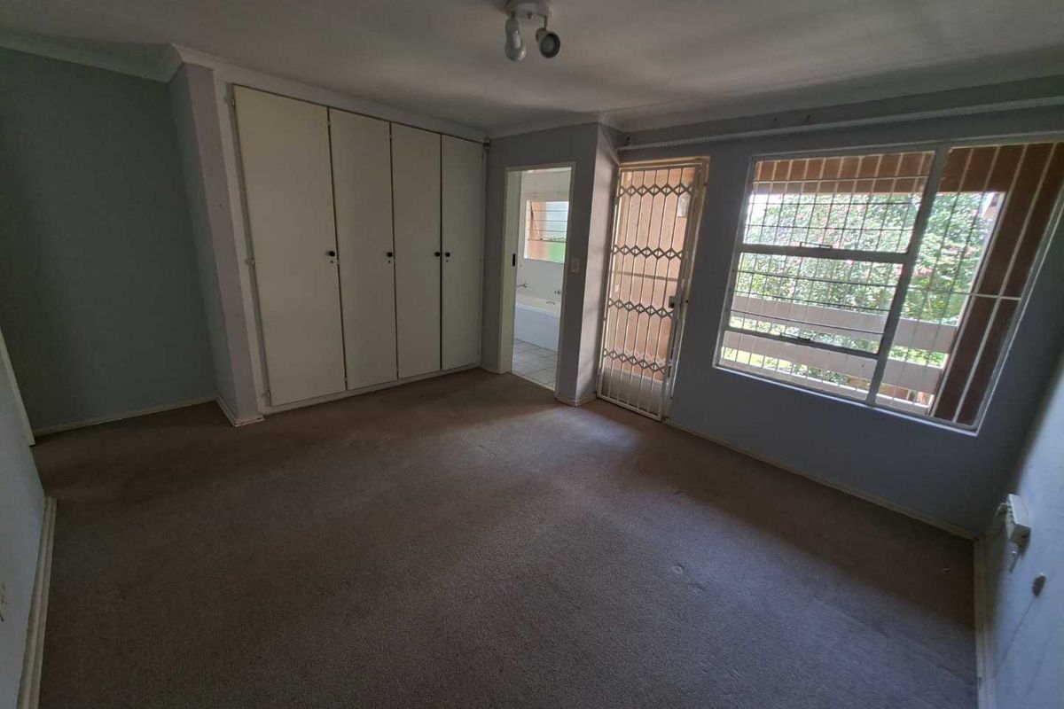 Spacious bedroom featuring built-in cupboards, carpeted flooring, and direct access to an en-suite bathroom, secured with a metal security gate and burglar bars.