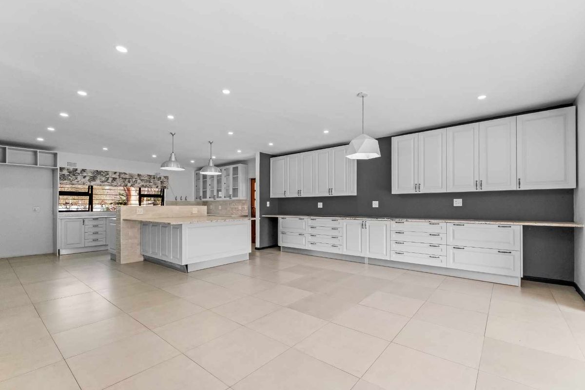 Spacious, modern kitchen featuring extensive white cabinetry, stone countertops, a central island, and neutral tiled flooring with recessed and pendant lighting.